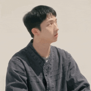 a young man wearing a black jacket is sitting in front of a wall .