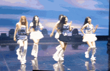 a group of girls are dancing on a stage with a blue sky in the background