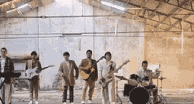 a group of men are standing in a warehouse playing guitars and drums .