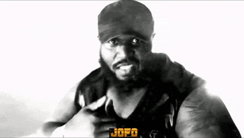a black and white photo of a man with a beard wearing a hat and a black tank top .