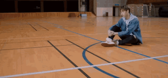 a man sits on the floor of a gym tying his shoelaces