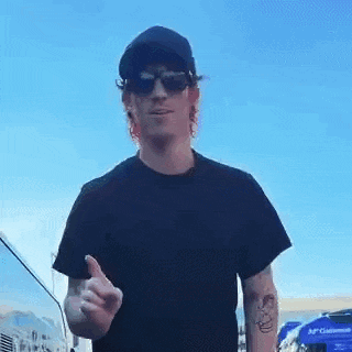 a man wearing sunglasses , a hat and a black shirt is giving the middle finger .