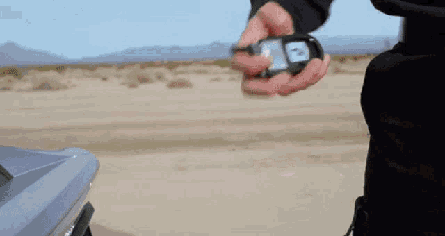 a man is standing next to a car in the desert holding a piece of paper .