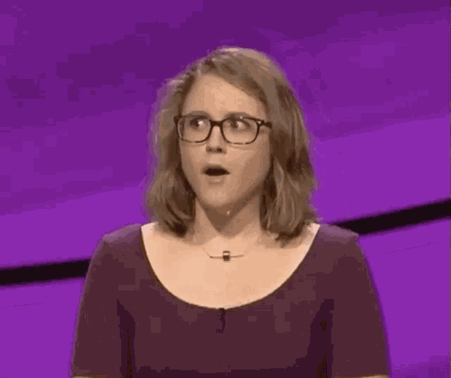a woman wearing glasses and a necklace is smiling on a purple background