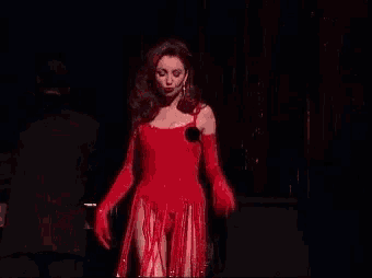 a woman in a red dress and gloves is standing on a stage .