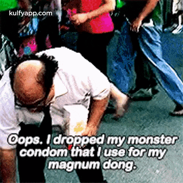a bald man is kneeling down on the street with a crowd behind him .