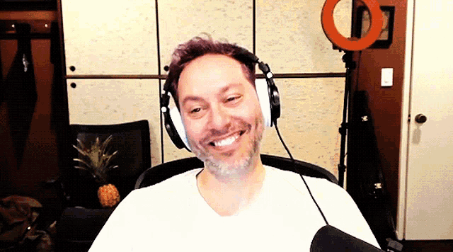 a man wearing headphones and a white shirt smiles for the camera