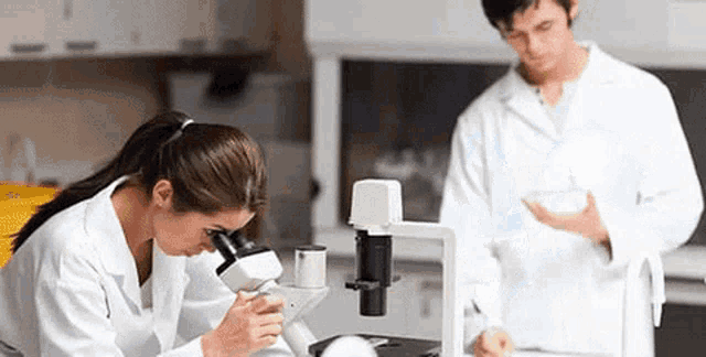 a man and a woman are looking through a microscope in a lab .