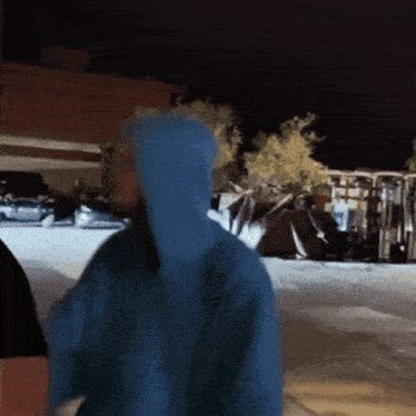 a person wearing a blue hoodie is standing in a parking lot at night