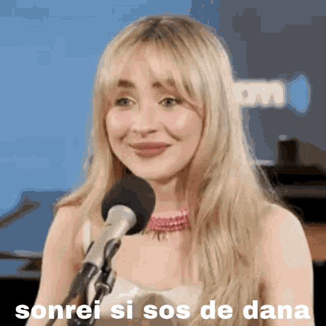 a woman is smiling in front of a microphone with the words sonrei si sos de dana written on the bottom