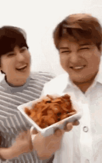 a man is holding a bowl of food next to another man who is holding a bowl of food .