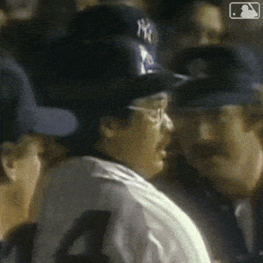 a man wearing a ny yankees hat and glasses is talking to another man .
