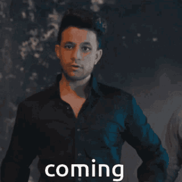 a man in a black shirt stands in front of a sign that says " coming "