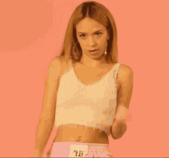 a woman wearing a white crop top and pink shorts is dancing on a pink background .