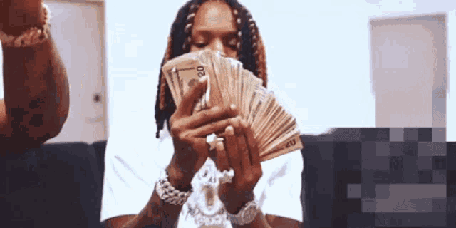 a man with dreadlocks is holding a bunch of money in front of his face .