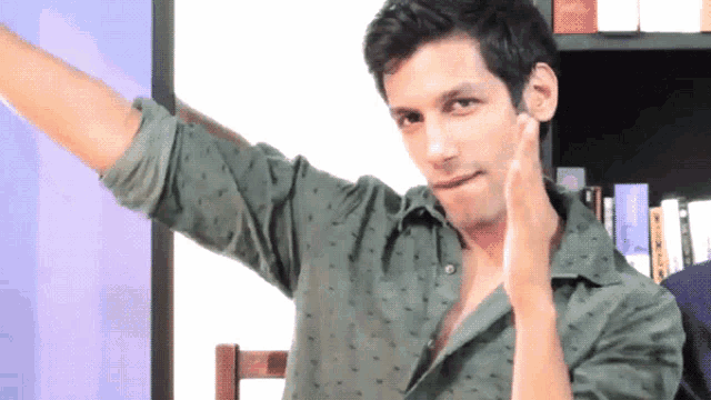 a man in a green shirt has his arm outstretched in front of a bookshelf