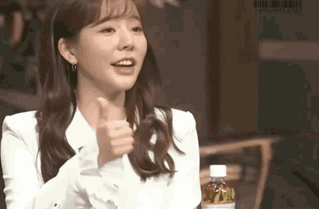 a woman in a white jacket is giving a thumbs up sign while sitting next to a bottle of water .