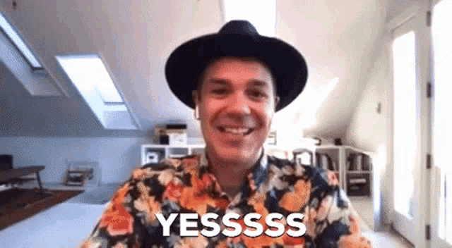 a man wearing a black hat and a floral shirt is smiling and says yesssss .