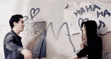a man and a woman are hugging in front of a wall with graffiti .