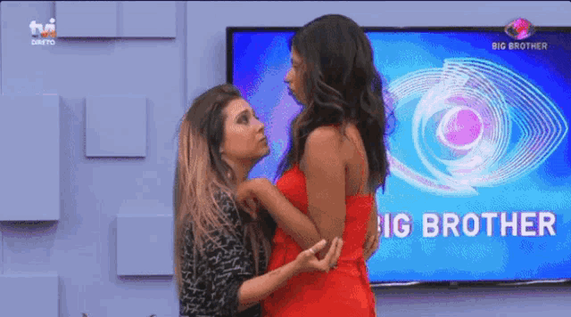 two women are standing in front of a big brother tv screen