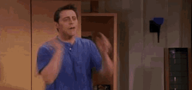 a man in a blue shirt is standing in a living room with his mouth open and a surprised look on his face .