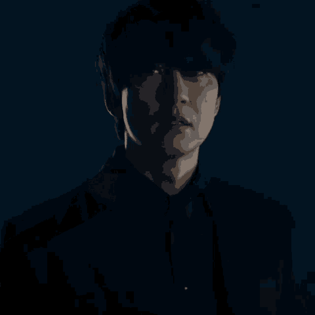 a man in a black suit and tie is standing in the dark looking at the camera .
