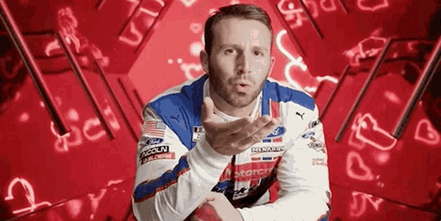 a man in a racing uniform is blowing a kiss in front of a red background .