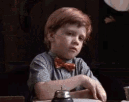 a young boy wearing a bow tie is sitting at a table with a bell on it