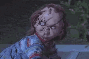 a chucky doll is sitting on a sidewalk in the dark looking at the camera .
