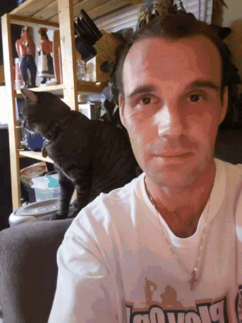 a man taking a selfie with a cat behind him wearing a shirt that says " cowboy "
