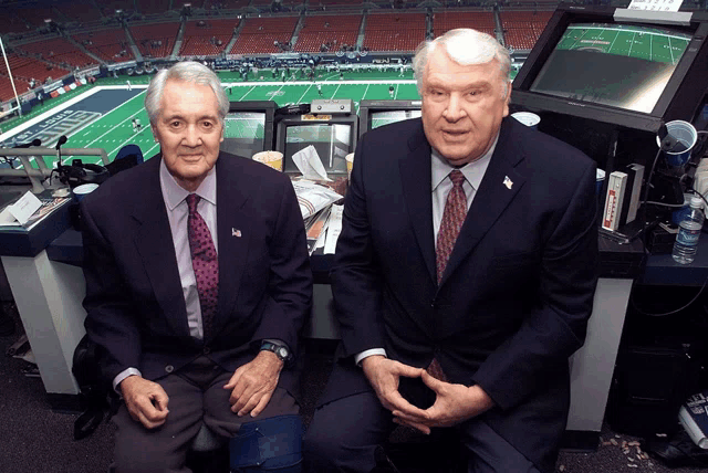 two men sit in a booth in front of a football field that says nfl