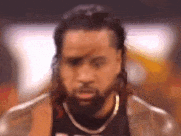 a close up of a man with a beard and long hair wearing a jacket and a necklace .