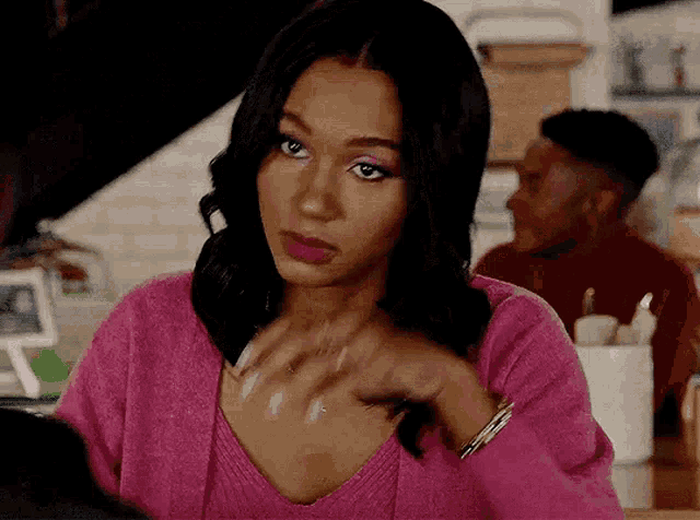 a woman in a pink sweater is sitting at a table with a man in a red shirt in the background .