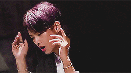 a young man with purple hair is making a gesture with his hands while wearing a suit .
