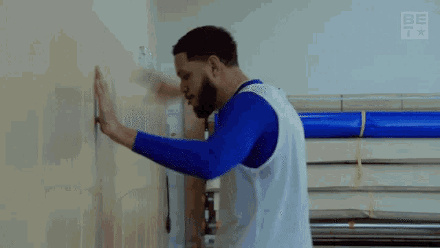 a man in a blue shirt and white vest is leaning against a wall