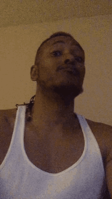 a man is wearing a white tank top and looking up