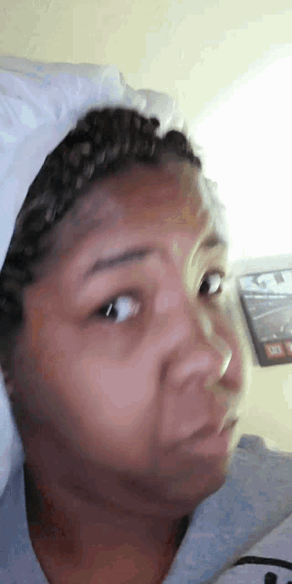 a woman laying in bed with a white pillow on her head looking at the camera