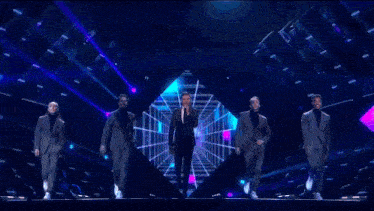 a group of men in suits are dancing on a stage in front of a blue light .