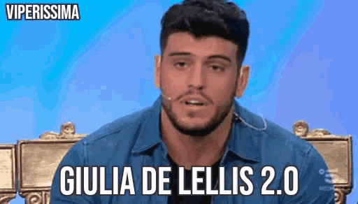 a man with a beard is sitting in front of a microphone with the words giulia de lellis 2.0 written below him .