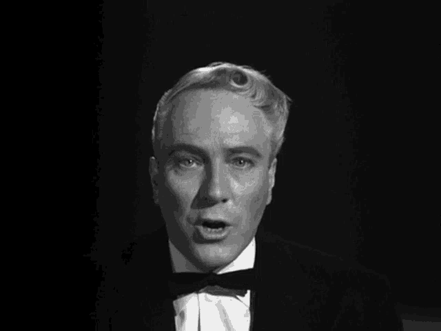 a man in a tuxedo and bow tie looks at the camera in a black and white photo