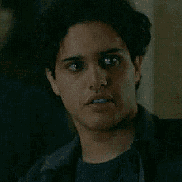 a close up of a man 's face with curly hair wearing a black shirt and jacket .