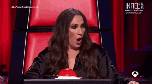 a woman is sitting in a chair with her mouth open and a red button in front of her ..