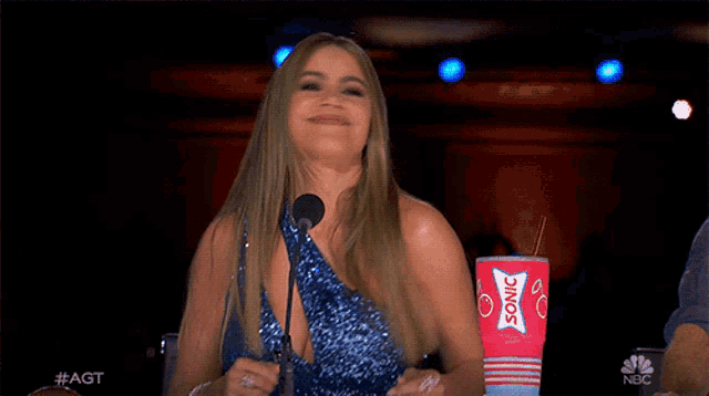 a woman in a blue sequined dress is holding a sonic cup