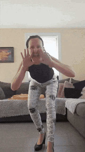 a woman in a black top and white pants is making a funny face