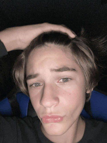 a young man with a hand on his head making a face