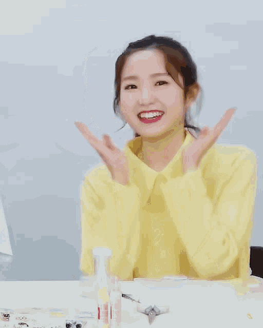 a woman in a yellow shirt is smiling with her hands on her chin