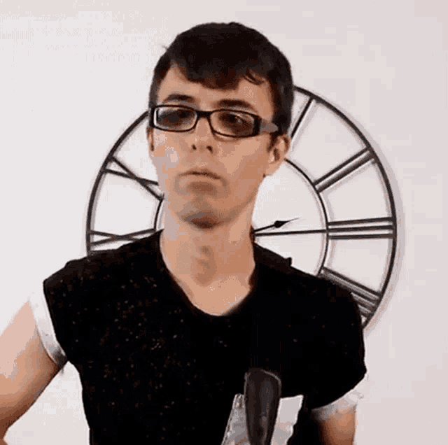 a man wearing glasses is standing in front of a clock .