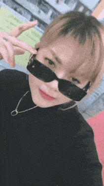 a woman wearing sunglasses and a black turtleneck is making a peace sign .
