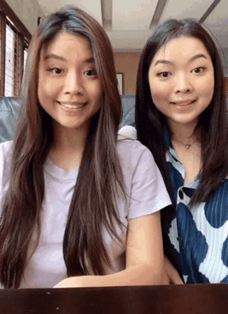 two girls are sitting next to each other and smiling at the camera .