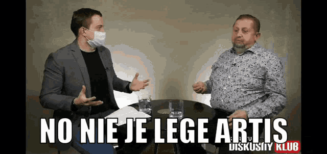 two men are sitting at a table and one of them is wearing a mask